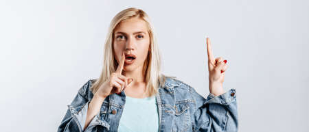 Look here. Young beautiful blonde woman points her fingers to the top thinks and makes a decision. The woman thought about the choice. Place for advertising.の写真素材