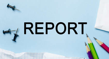 Text REPORT on a white notepad with pencils on a blue background. Business conceptの写真素材