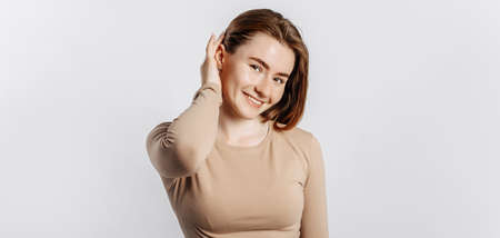 Beautiful young girl smiling and posing looking at the camera on a white isolated background. Positive brunette woman in a beige jumper. Kind look.の写真素材