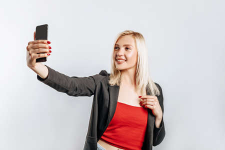 Beautiful young cute girl smiling and holding phone on gray isolated backgroundの写真素材