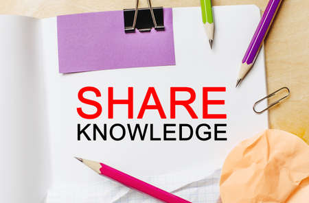 Text SHARE KNOWLEDGE on a white notepad with pencils on a wooden background. Business conceptの写真素材