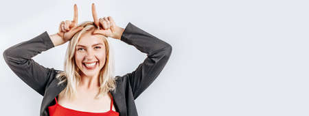 Beautiful young cute girl smiling fooling around and making horns gesture on gray isolated backgroundの写真素材