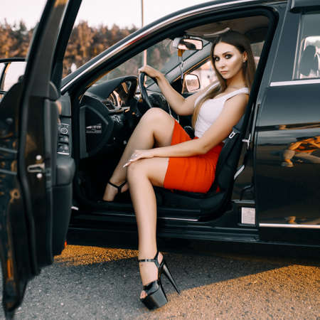 Beautiful young girl driving a car in the evening in the sunset sun on an empty parking lotの写真素材
