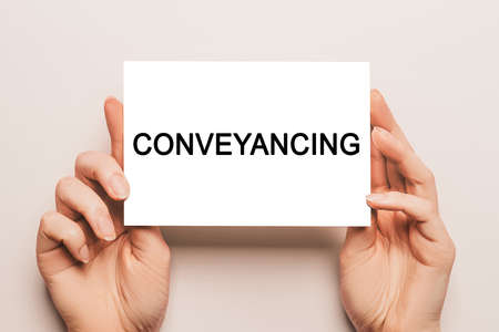 Female hands hold card paper with text Conveyancing on a yellow background. Business and finance conceptの写真素材
