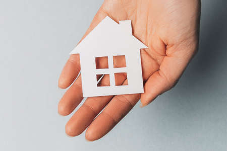 Woman holding a paper house with her hands with the sun on a light blue background. Sweet homeの写真素材
