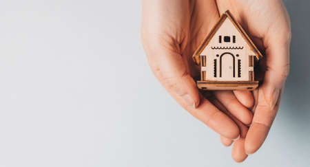 Woman holding a wooden house with her hands with the sun on a light blue background. Sweet homeの写真素材