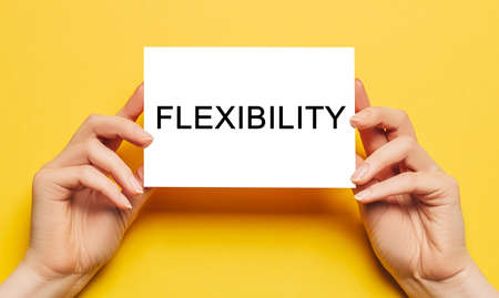 Female hands hold card paper with text Flexibility on a yellow background. Business and finance conceptの写真素材