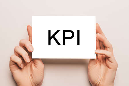 Female hands hold card paper with text KPI on a yellow background. Business and finance conceptの写真素材