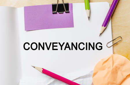 Text Conveyancing on a white notepad with pencils on a wooden background. Business conceptの写真素材