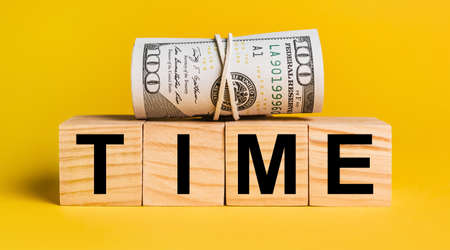 TIME with money on a yellow background. The concept of business, finance, credit, income, savings, investments, exchange, taxの写真素材