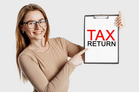 Tax return. Beautiful young business woman wearing glasses holds a clipboard with mock up space isolated on gray backgroundの写真素材