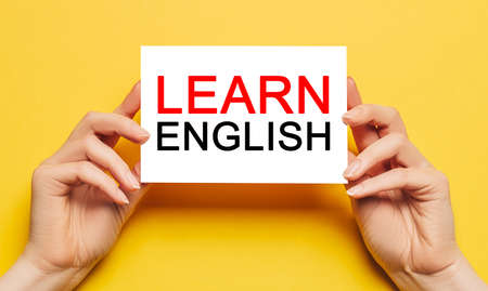 Female hands hold card paper with text Learn ENGLISH on a yellow background. Education and language conceptの写真素材