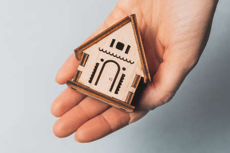 Woman holding a wooden house with her hands with the sun on a light blue background. Sweet homeの写真素材