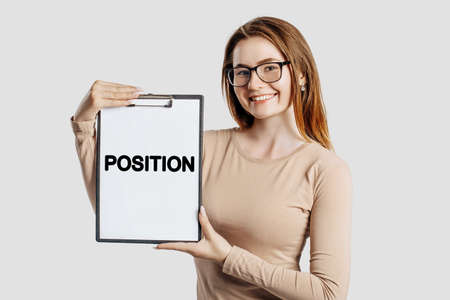 POSITION. Beautiful young business woman wearing glasses holds a clipboard with mock up space isolated on gray backgroundの写真素材