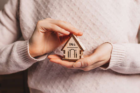 Woman holding a wooden house with her hands with the sun on a light pink background. Sweet homeの写真素材