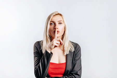 Beautiful young serious girl showing hush gesture, keep secret on gray isolated backgroundの写真素材