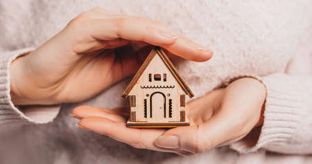 Woman holding a wooden house with her hands with the sun on a light pink background. Sweet homeの写真素材