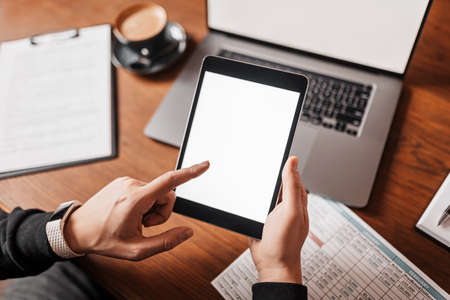 Male hands holding tablet with blank background at workplace. Businessman working at his desk with documentsの写真素材