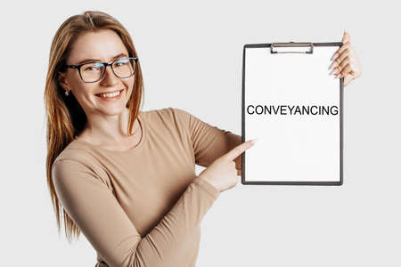Conveyancing. Beautiful young business woman wearing glasses holds a clipboard with mock up space isolated on gray backgroundの写真素材