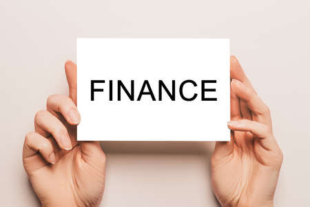 Female hands hold card paper with text FINANCE on a yellow background. Business and finance conceptの写真素材