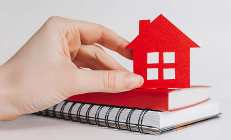 Sweet home. Estimating and paying house tax. Woman holding red house with her hands and notepad in copy space white backgroundの写真素材
