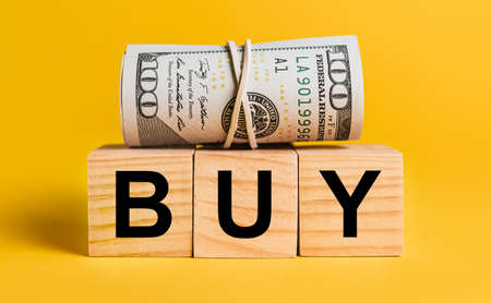 BUY with money on a yellow background. The concept of business, finance, credit, income, savings, investments, exchange, taxの写真素材