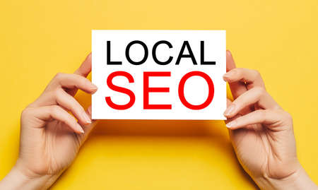 Female hands hold card paper with text LOCAL SEO on a yellow background. Business and finance conceptの写真素材