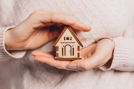 Woman holding a wooden house with her hands with the sun on a light pink background. Sweet homeの写真素材
