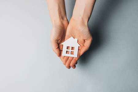 Woman holding a paper house with her hands with the sun on a light blue background. Sweet homeの写真素材