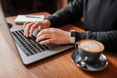 Handsome man working on laptop in the workplace. Businessman prints information at desk with coffeeの写真素材