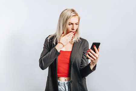 Beautiful young girl unhappy and holding phone on gray isolated backgroundの写真素材