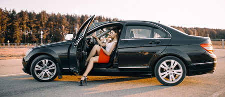 Beautiful young girl driving a car in the evening in the sunset sun on an empty parking lotの写真素材