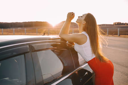 Beautiful young girl near a car in the evening in the sunset sun in an empty parking lotの写真素材