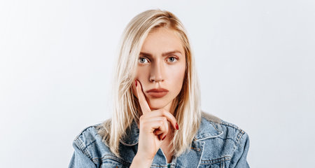 The woman thought about the choice and furrowed her eyebrows. Young beautiful blonde girl holds a finger to the face thinks and makes a decision. Place for advertising. What to chooseの写真素材