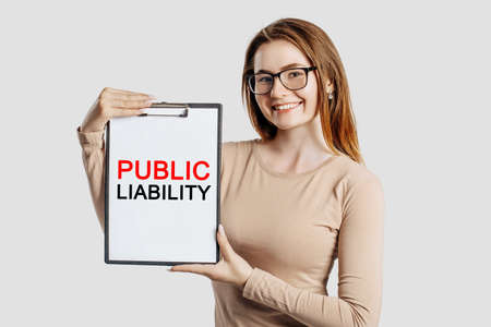 PUBLIC LIABILITY. Beautiful young business woman wearing glasses holds a clipboard with mock up space isolated on gray backgroundの写真素材