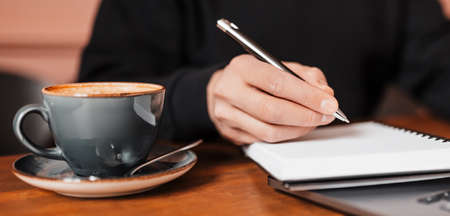 Handsome man working on laptop in the workplace. Businessman typing information on computer at work table with coffee and notepadの写真素材