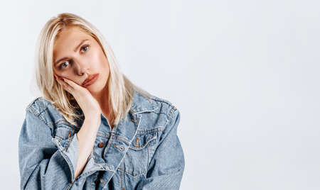 The woman thought about the choice and furrowed her eyebrows. Young beautiful blonde girl holds a hand to the face thinks and makes a decision. Place for advertising. What to chooseの写真素材