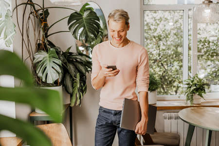 Man checks the phone, businessman with laptop in workspace in eco cafe with plantsの写真素材