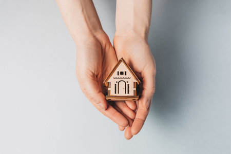 Woman holding a wooden house with her hands with the sun on a light blue background. Sweet homeの写真素材