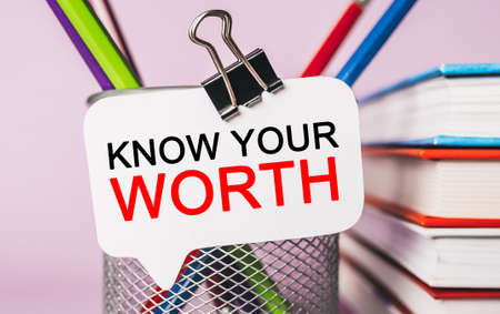 Text KNOW YOUR WORTH on a white sticker with office stationery background. Flat lay on business, finance and development conceptの写真素材