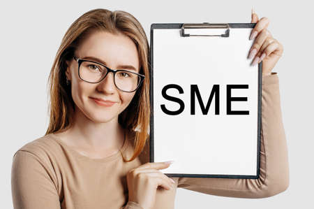 sme. Beautiful young business woman wearing glasses holds a clipboard with mock up space isolated on gray backgroundの写真素材