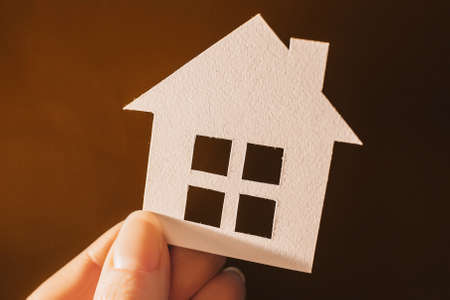 Woman holding a paper house with her hands backlit on a dark background. Sweet homeの写真素材