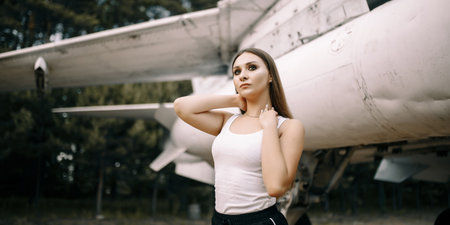 beautiful young brunette girl stands on the background of old military aircraft. Girl in a white...
