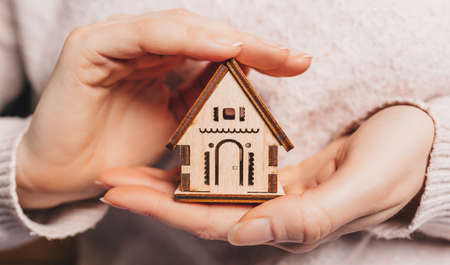 Woman holding a wooden house with her hands with the sun on a light pink background. Sweet homeの写真素材