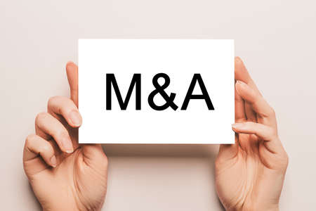 Female hands hold card paper with text M and A on a yellow background. Business and finance conceptの写真素材