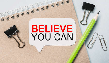 Text Believe you can on a white sticker with office stationery background. Flat lay on business, finance and development conceptの写真素材