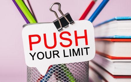Text PUSH YOUR LIMIT on a white sticker with office stationery background. Flat lay on business, finance and development conceptの写真素材