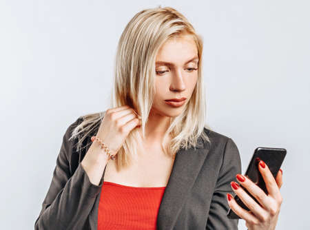 Beautiful young girl unhappy and holding phone on gray isolated backgroundの写真素材
