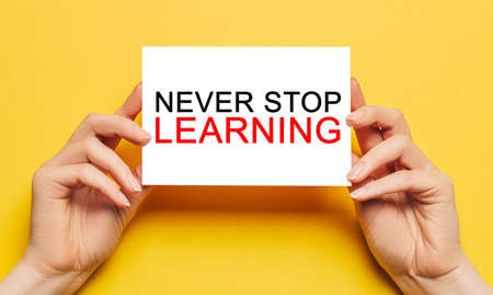 Female hands hold card paper with text Never Stop Learning on a yellow background. Education and study conceptの写真素材