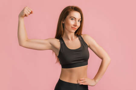 Fitness girl smiling in black sportswear on a pink background. Slim woman with a beautiful athletic body and tanned skinの写真素材